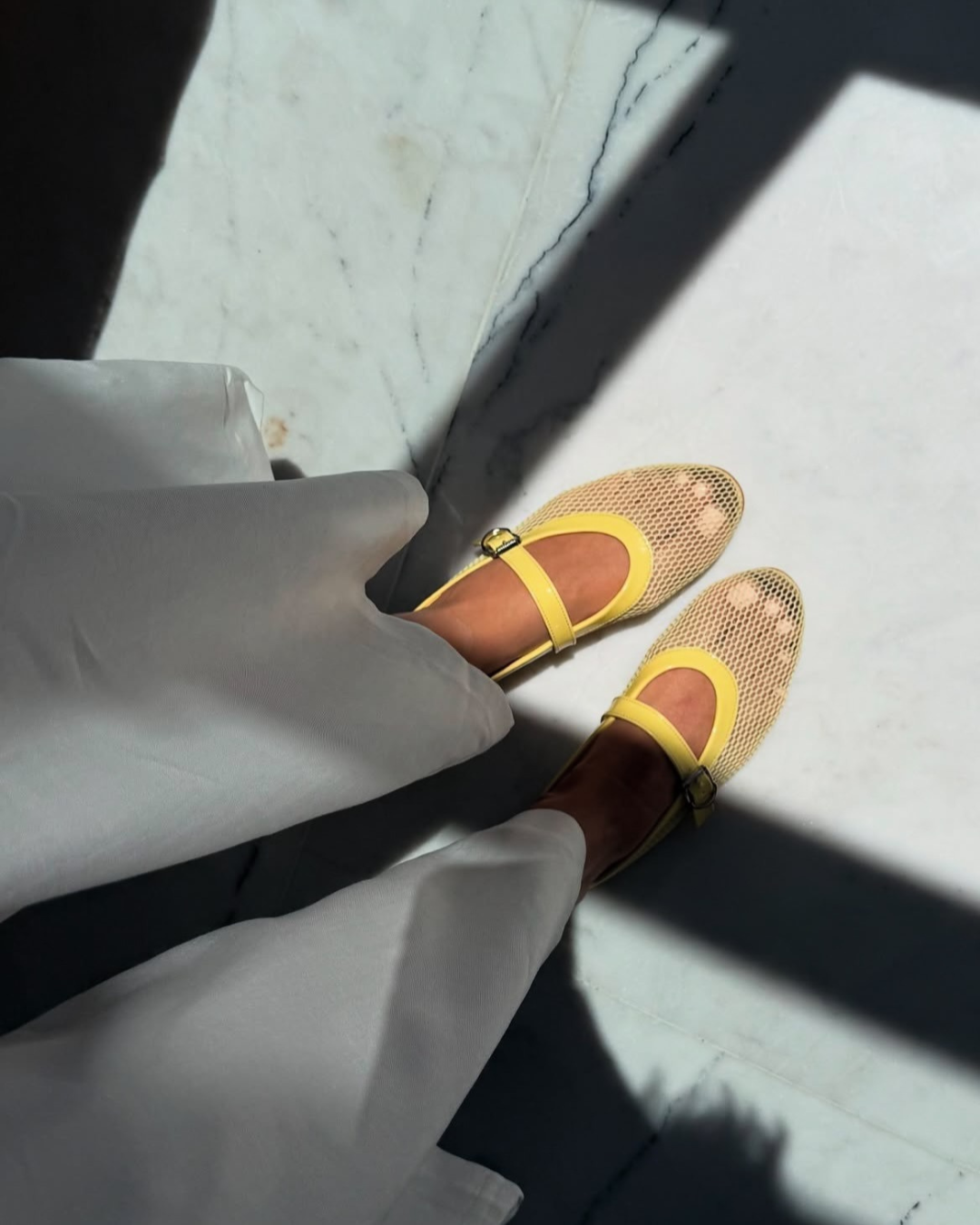 Yellow and brown open-toe shoes on a marble floor with a white garment.