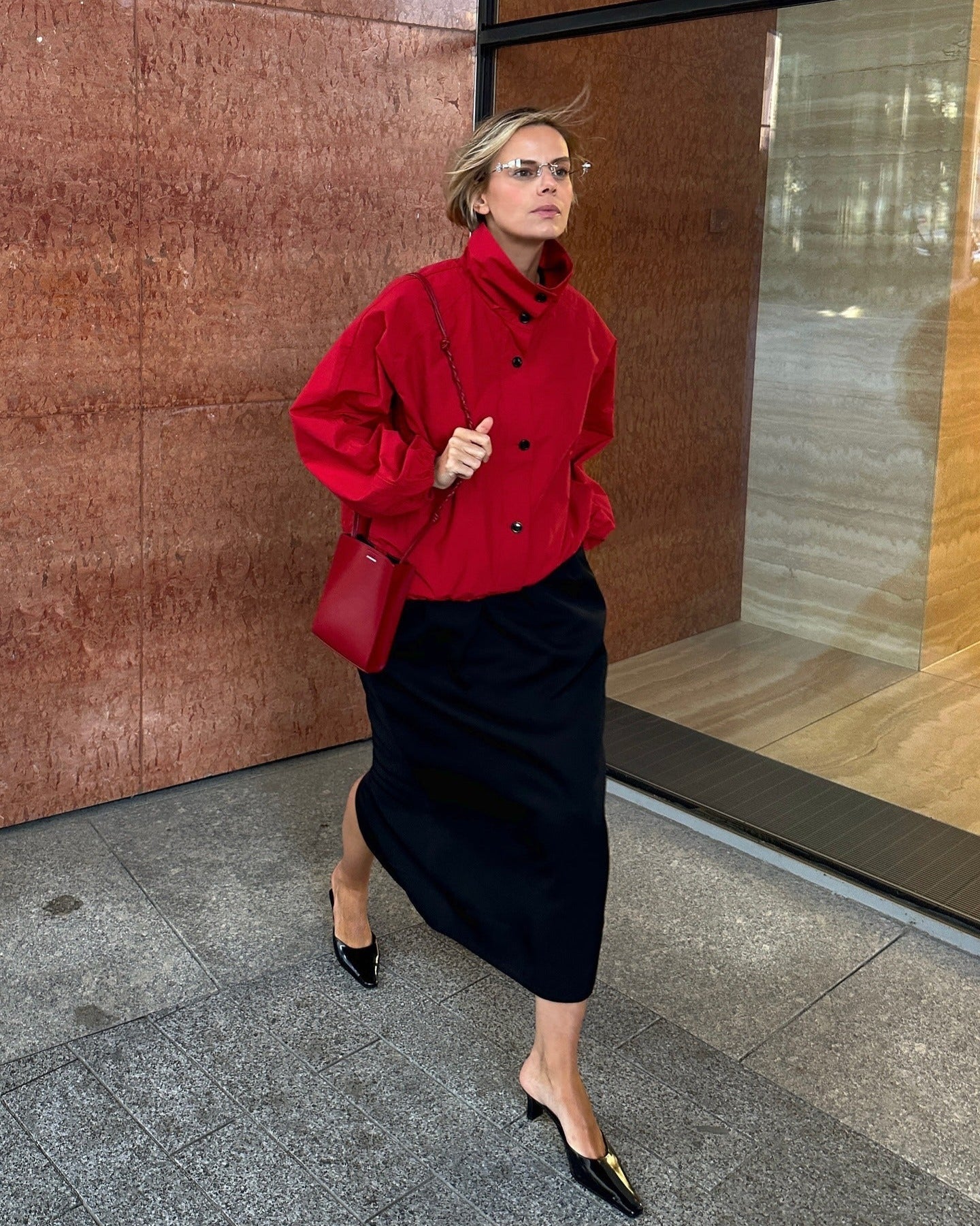 Woman in a red coat and black skirt standing in front of a building entrance.