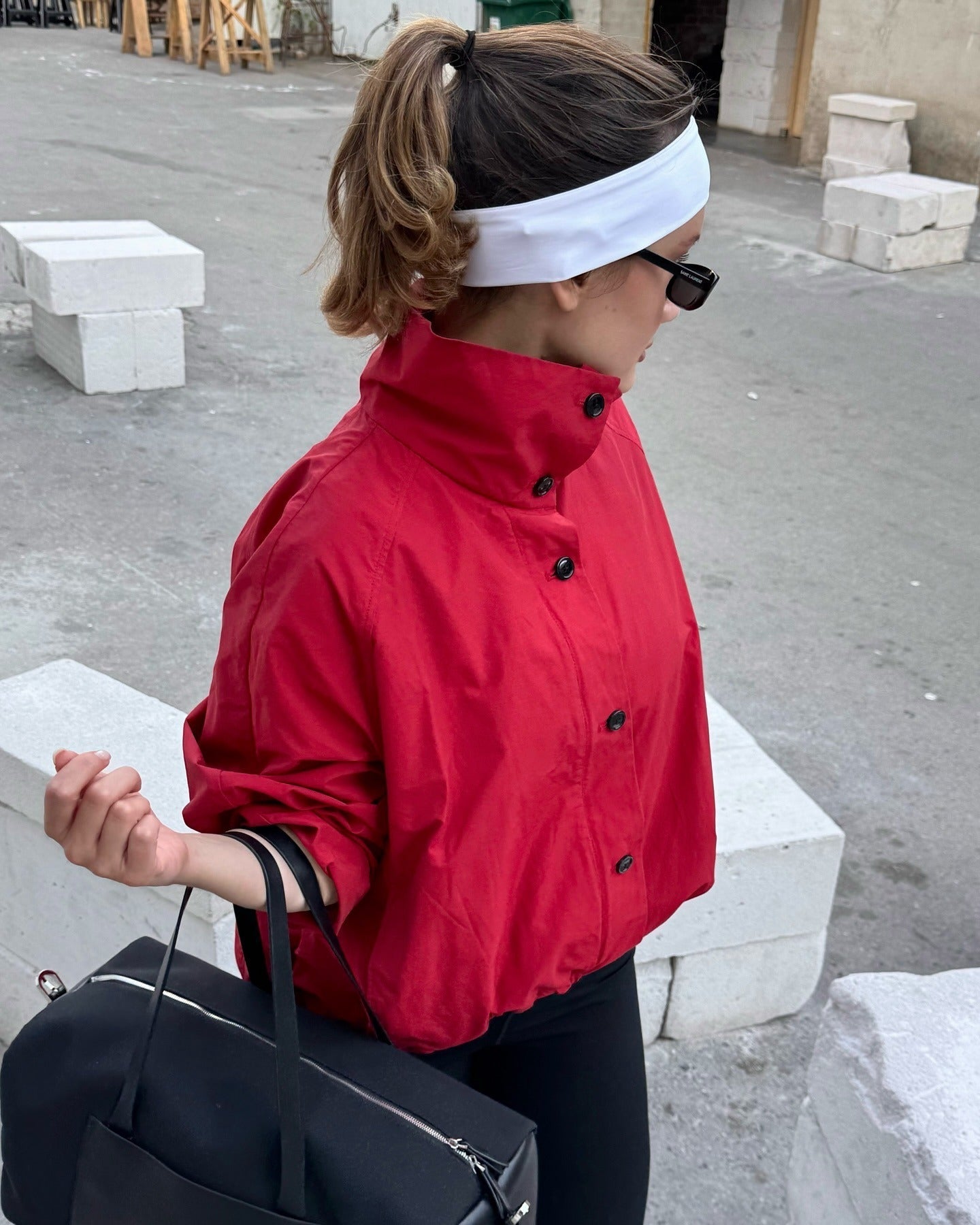 Person wearing a red jacket and white headband outdoors on a concrete surface.